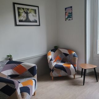 Hypnose et Constellations familiales à Chambéry Coin salon avec deux fauteuils colorés, une table basse et un tableau au mur.